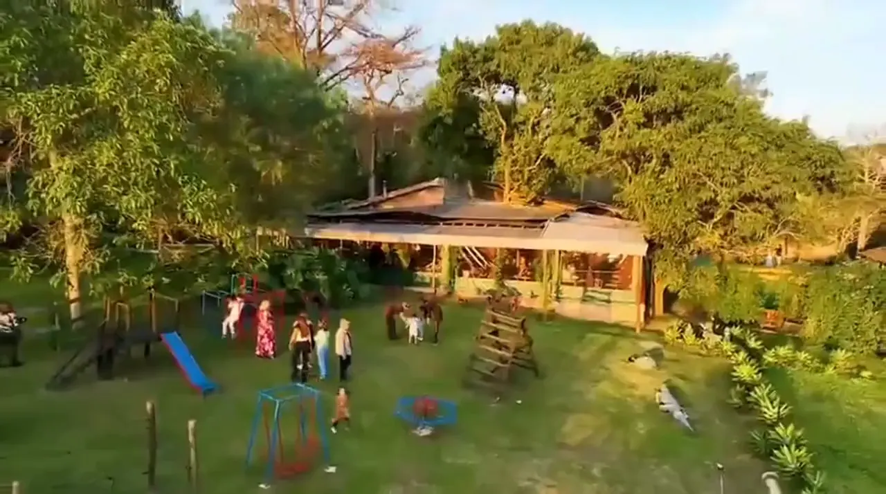 Vista aérea do Sítio Doce Campo no fim da tarde: a casa do restaurante entre árvores, o gramado e o parquinho